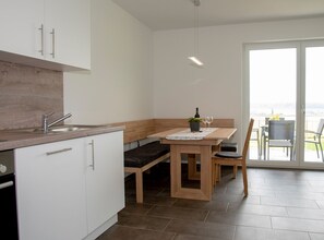 Une cuisine moderne avec des meubles blancs, un plan de travail en bois et un coin repas comprenant un banc et une table.