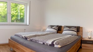 Un dormitorio moderno con una cama de madera, una mesita de noche, una lámpara de noche y una ventana con vistas a árboles.