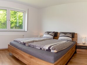 Une chambre moderne avec un lit en bois, une table de chevet, une lampe de chevet et une fenêtre donnant sur des arbres.