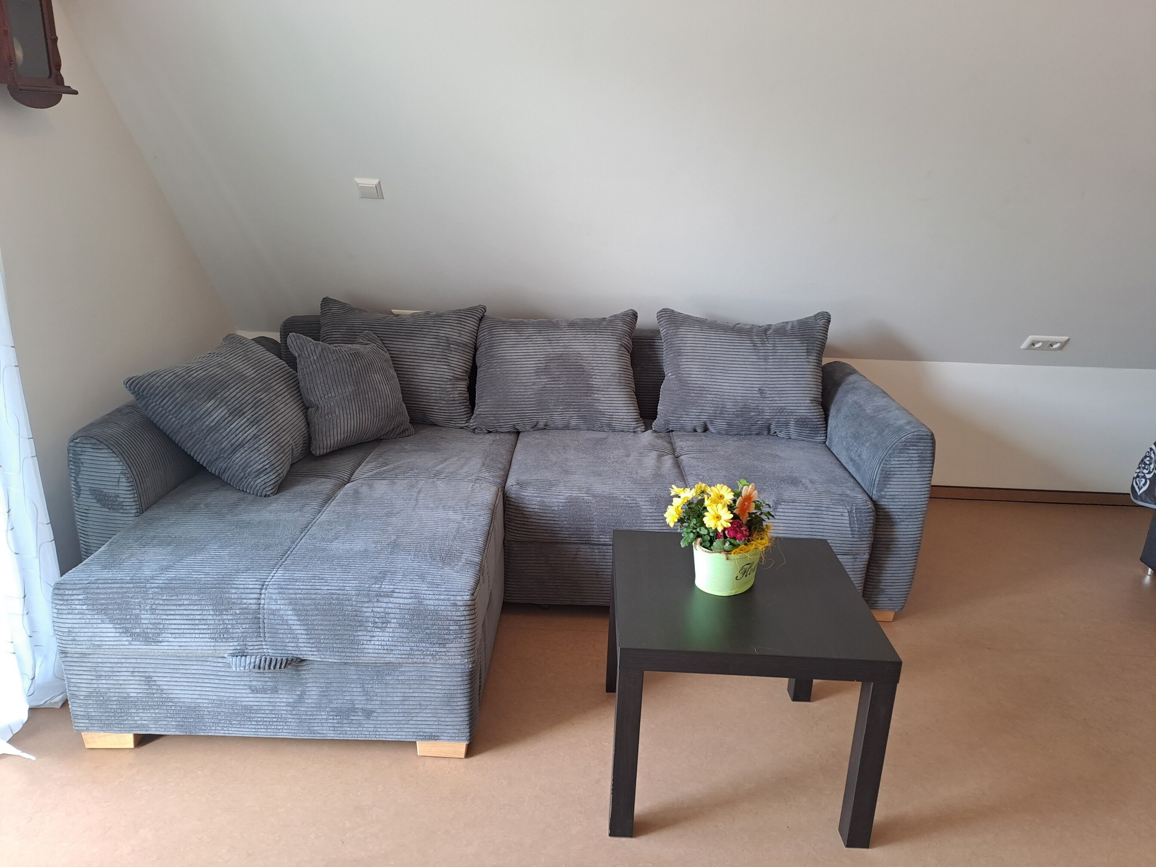 A grey sectional sofa with wooden legs, a black coffee table, and a vase with flowers.