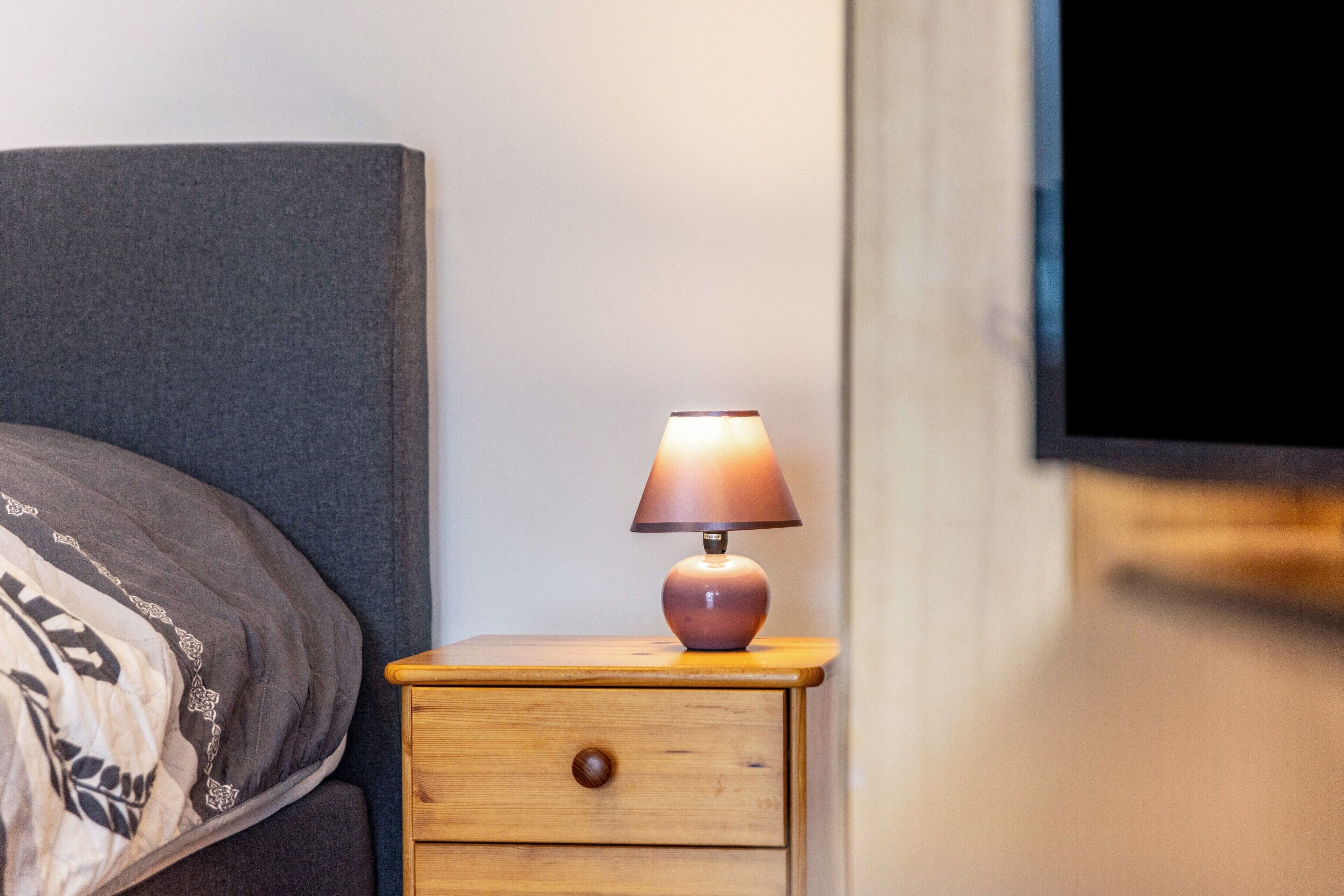 A bedside table with a lamp, a drawer, and a bed with a headboard.