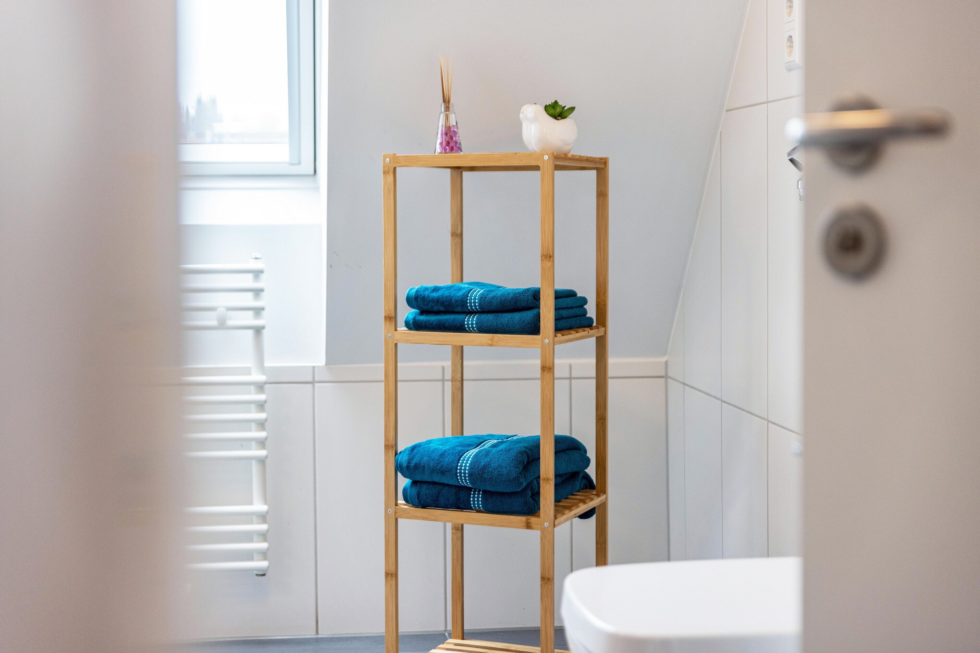 A bathroom with a wooden shelf holding towels, a white toilet, and a window with a view.