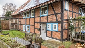 A traditional half-timbered house with a brick facade, multiple windows, and a small garden area with a wooden table and chairs. - Holiday Apartment 'Alte Polsterei' with Private Terrace, Shared Garden and Wi-Fi (Nienstädt)