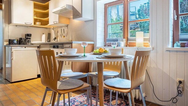 A modern kitchen with white cabinets, a dining table with chairs, and a window with a view of greenery. - Holiday Apartment 'Alte Polsterei' with Private Terrace, Shared Garden and Wi-Fi (Nienstädt)