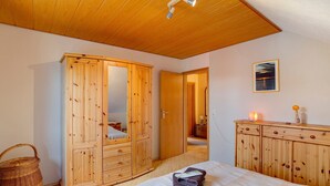Un dormitorio con un armario de madera, una cama con edredón blanco, techo de madera y un cuadro enmarcado en la pared.