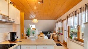 Una cocina moderna con una isla central, techo de madera y ventanas grandes con cortinas.