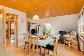 A spacious living area with a dining table, chairs, a sofa, and a television.