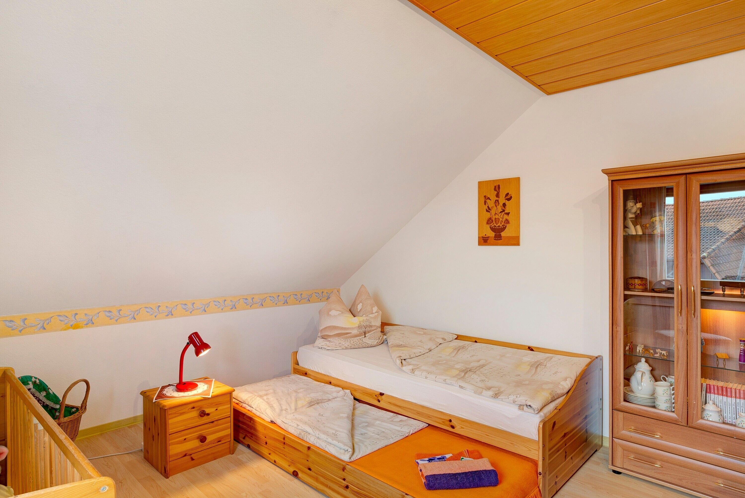 A bedroom with a loft bed, a small bedside table with a lamp, a wooden cabinet, and a patterned wall border.