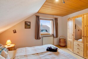 A bedroom with a bed, a window with curtains, a wooden wardrobe, a lamp, and a radiator.