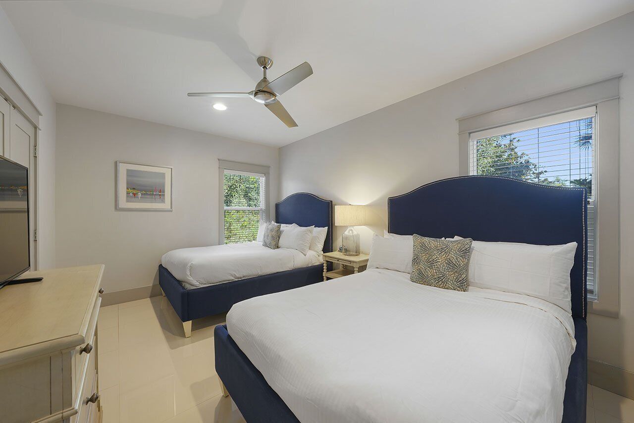 A bedroom with two beds, a ceiling fan, a nightstand with a lamp, and a window with blinds.