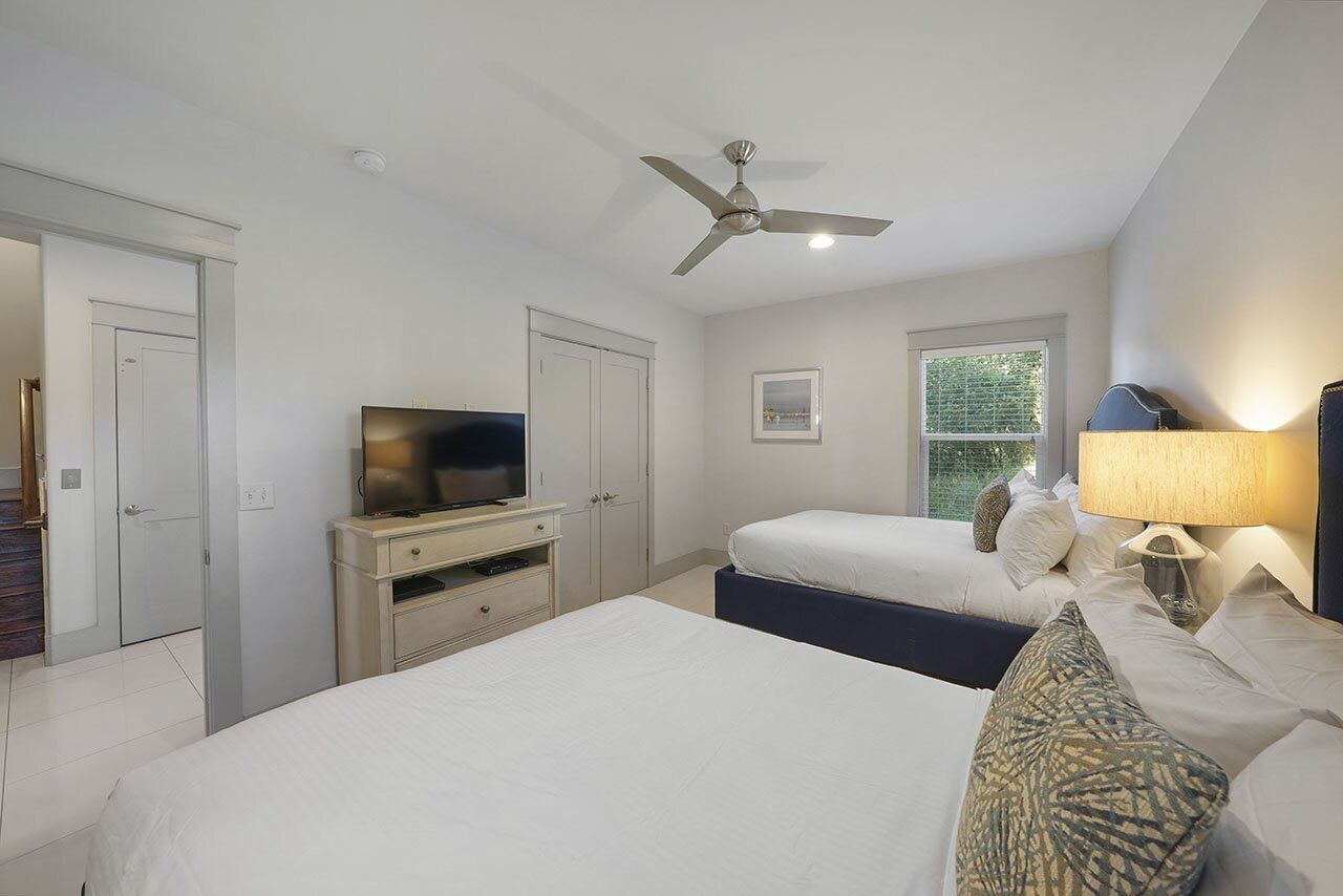 A hotel room with a bed, a TV, a ceiling fan, a window, and a lamp.