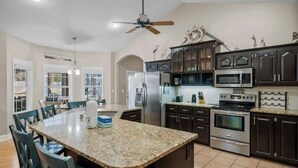 A spacious kitchen with granite countertops, dark cabinetry, stainless steel appliances, and a central island with seating.