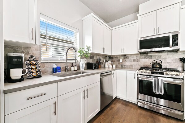 A modern kitchen with white cabinets, a coffee maker, a microwave, and an oven.