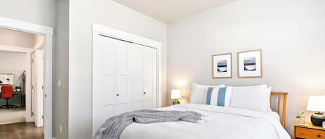 A bedroom with a bed, a nightstand with a lamp, two framed pictures on the wall, and a closet with a door.
