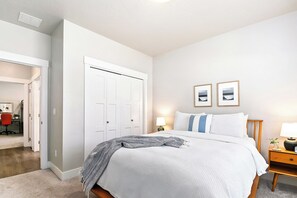 A bedroom with a bed, a nightstand with a lamp, two framed pictures on the wall, and a closet with a door.