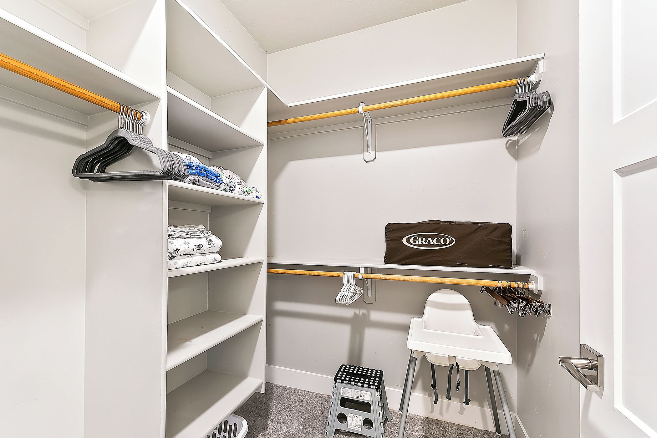 Un vestidor con estantes, una sillita de bebé Graco y un taburete.