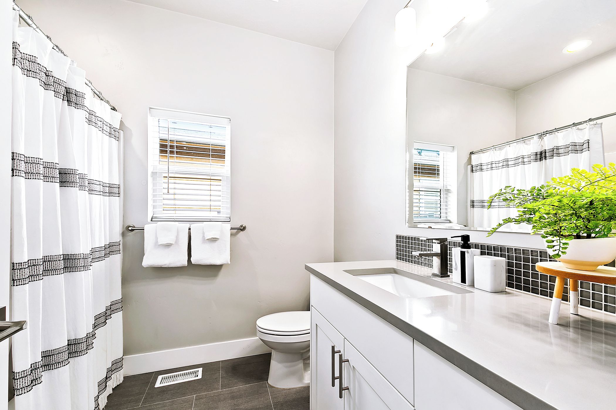 A modern bathroom with a white toilet, a shower curtain with a black pattern, a sink with a mirror, and a potted plant.