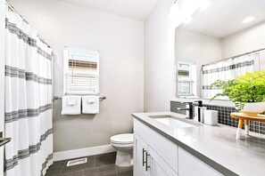A modern bathroom with a white toilet, a shower curtain with a black pattern, a sink with a mirror, and a potted plant.