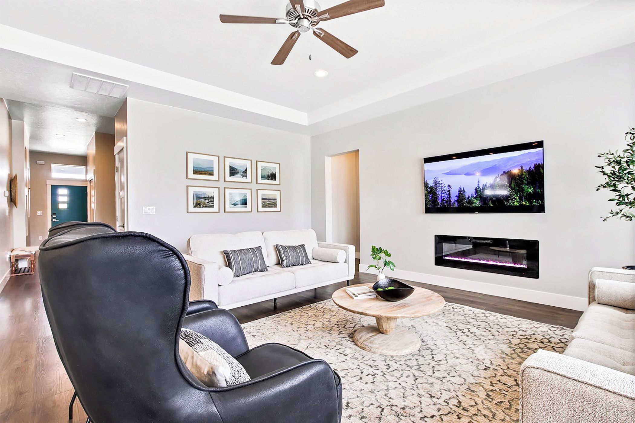 Un salon moderne avec un canapé blanc, un fauteuil en cuir noir et un téléviseur à écran plat fixé au mur.