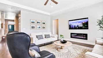 Un salon moderne avec un canapé blanc, un fauteuil en cuir noir et un téléviseur à écran plat fixé au mur.