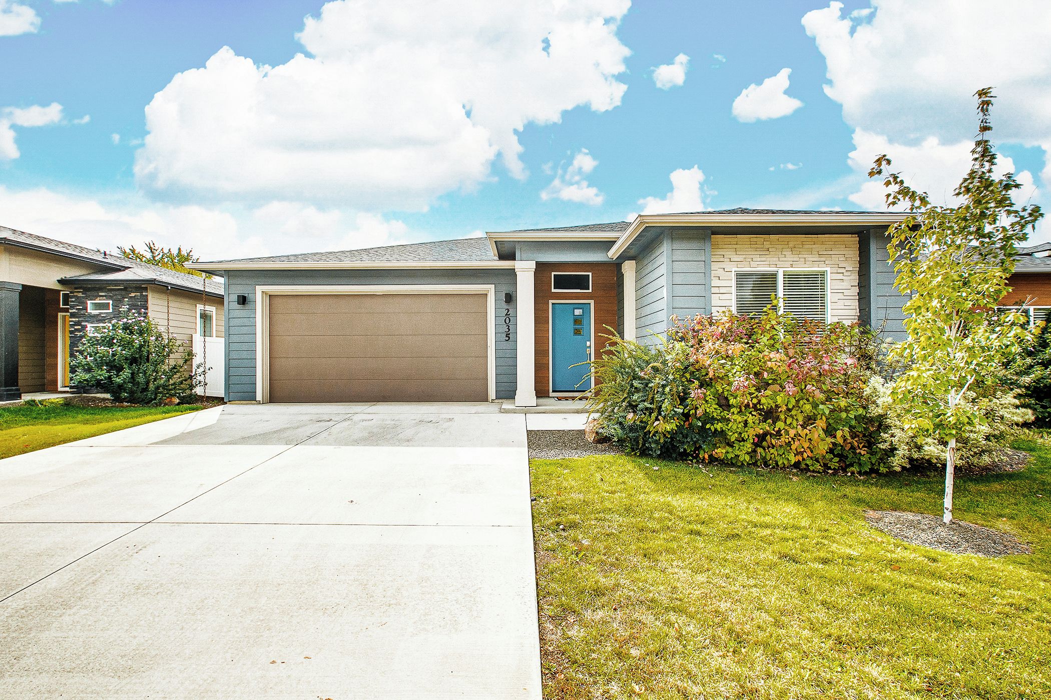 A residential house with a garage, a front yard with grass and shrubs, and a clear sky.