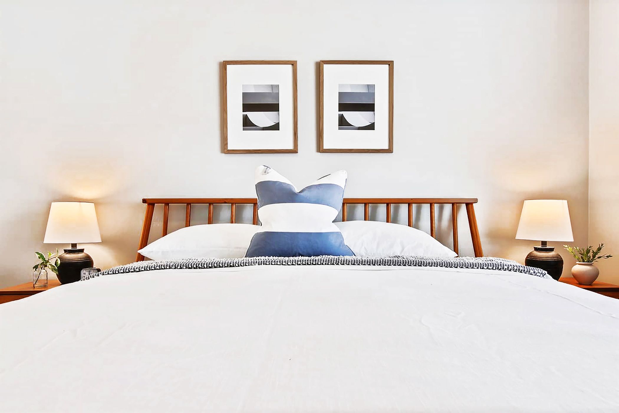 A neatly made bed with a white comforter and blue accent pillows, flanked by two bedside lamps and a small potted plant.