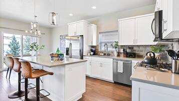 A modern kitchen with white cabinetry, a central island with bar stools, stainless steel appliances, and a view of the outdoors.