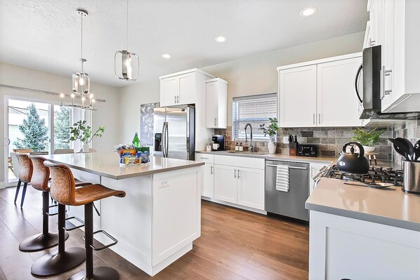 A modern kitchen with white cabinetry, a central island with bar stools, stainless steel appliances, and a view of the outdoors.