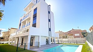 A modern multi-story building with a swimming pool in front. - Anacasa Macomer Oliva Playa AP803 (Oliva)