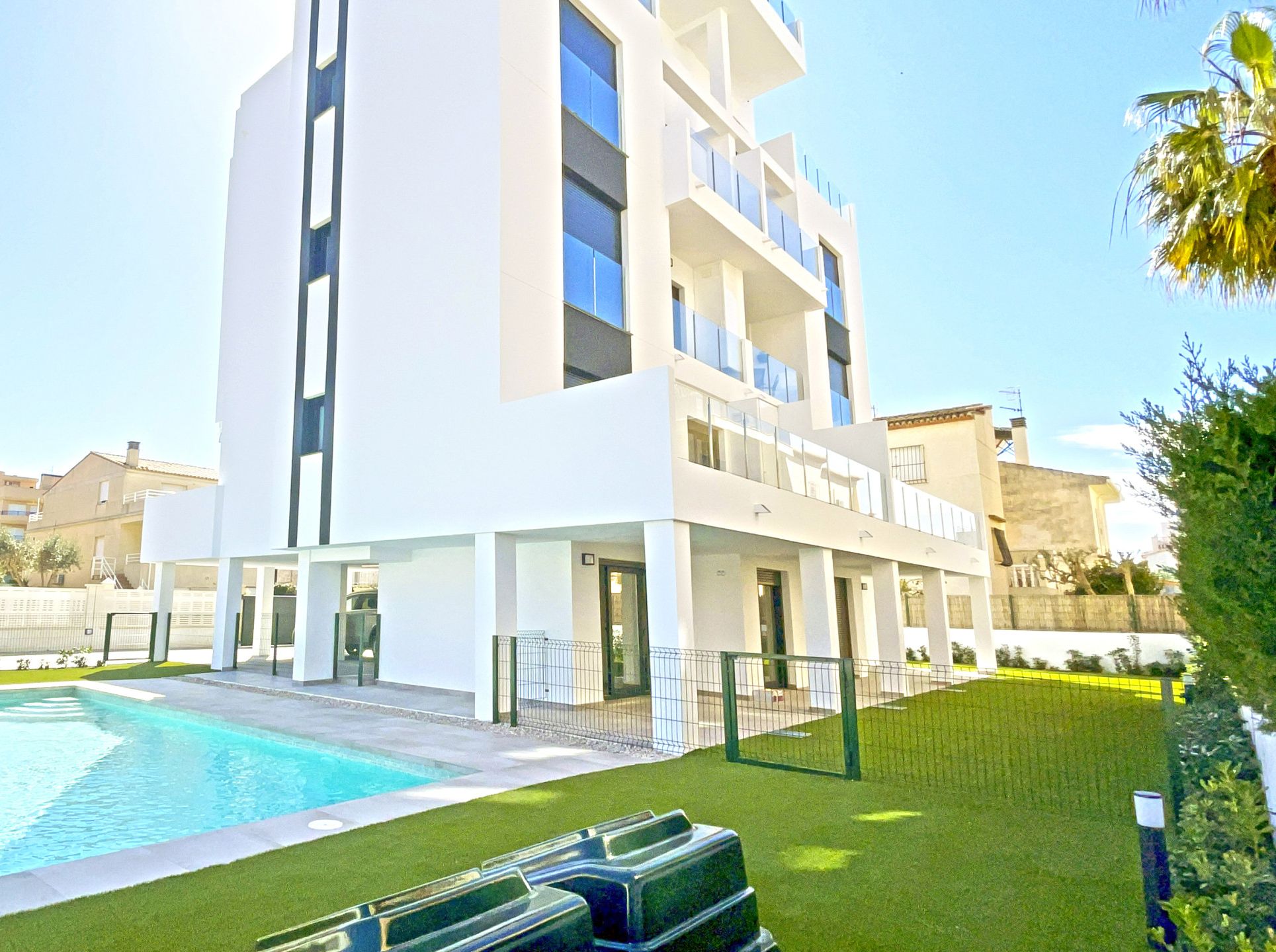 A modern building with a swimming pool, surrounded by a well-maintained lawn and a fence.