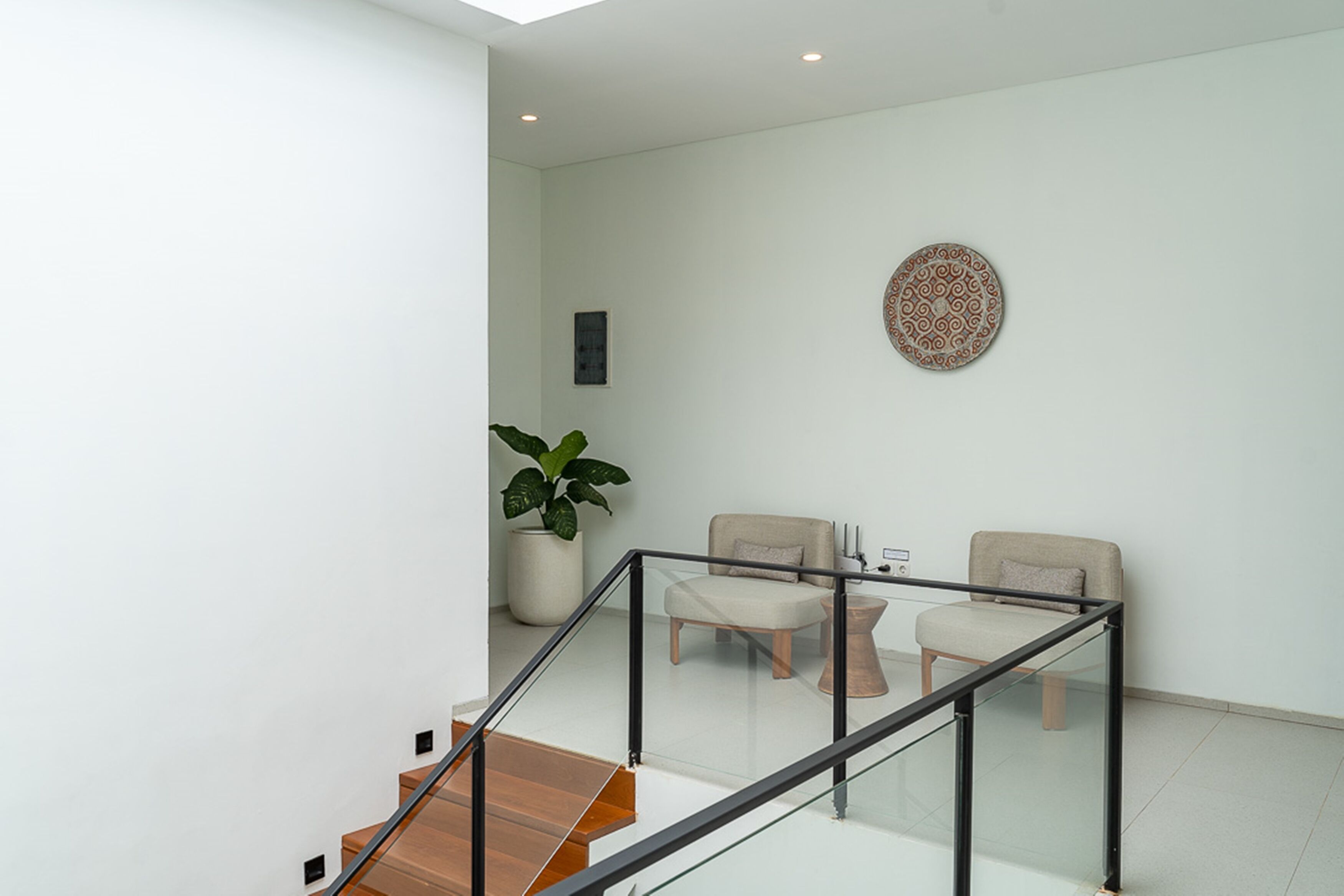 Un interior moderno con una escalera, dos sillas, una mesita y una planta en maceta.