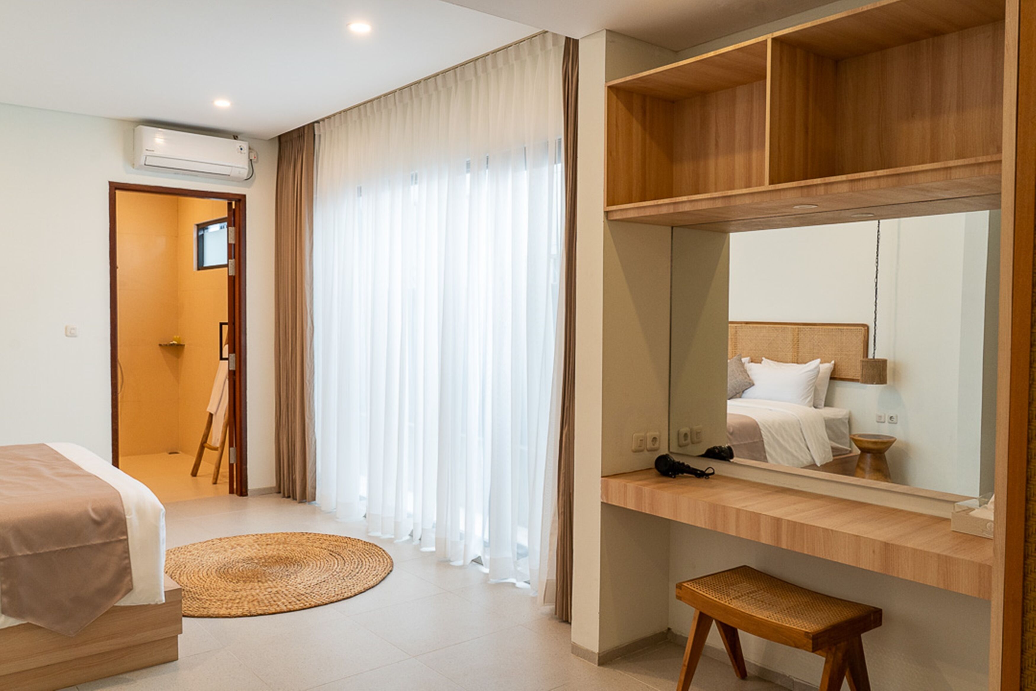 Une chambre d’hôtel avec un lit, un bureau et une chaise, un miroir et une grande fenêtre avec des rideaux.