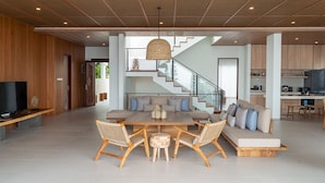 Un vaste espace de vie comprenant une grande table à manger en bois, des sièges confortables, un escalier et une cuisine à l’arrière-plan.