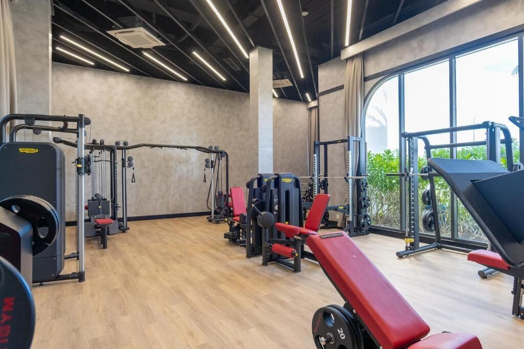 A gym with various exercise equipment, large windows, and a wooden floor.