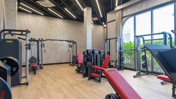A gym with various exercise equipment, large windows, and a wooden floor.