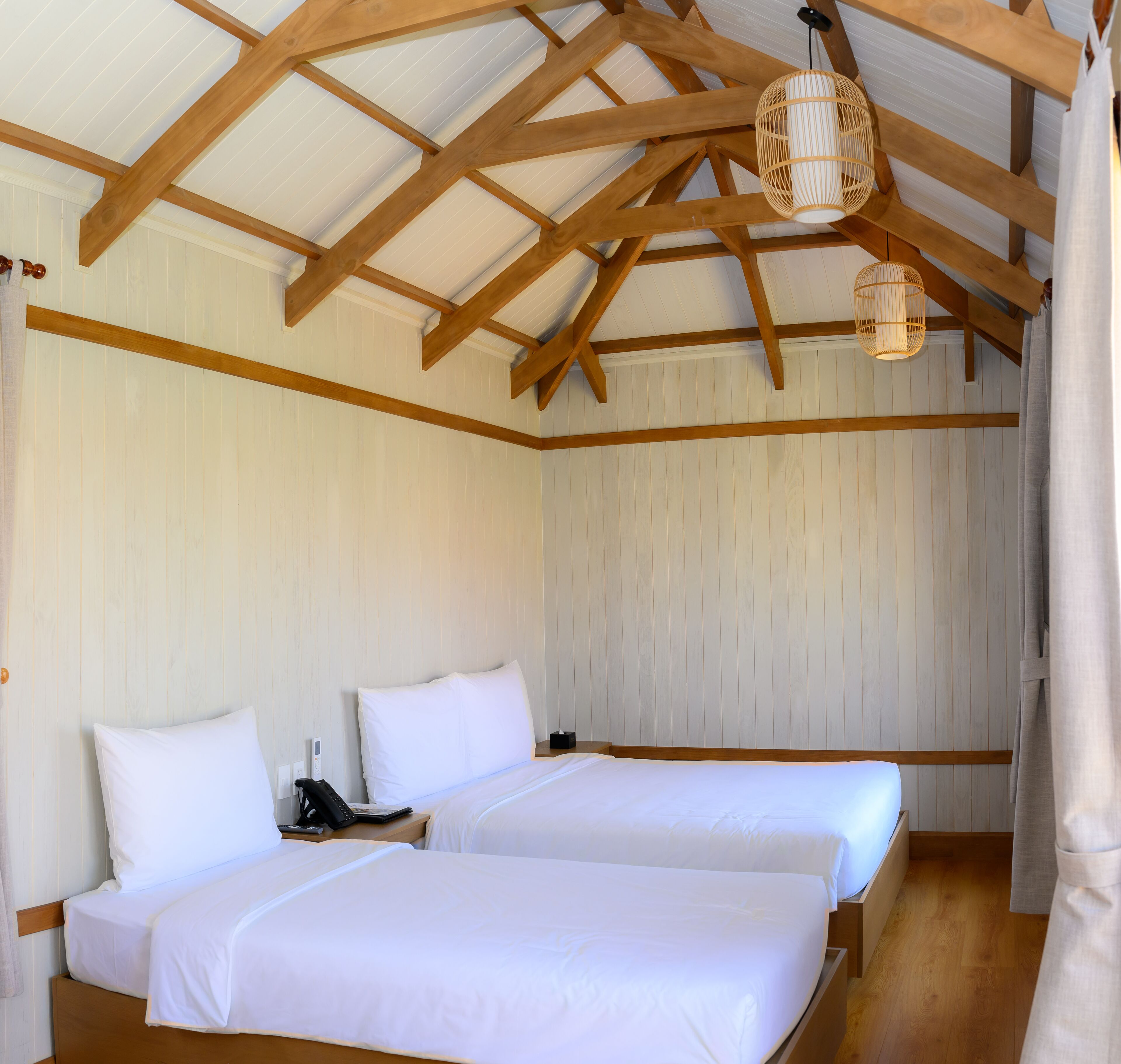 A room with two beds, wooden beams on the ceiling, and a hanging light fixture.