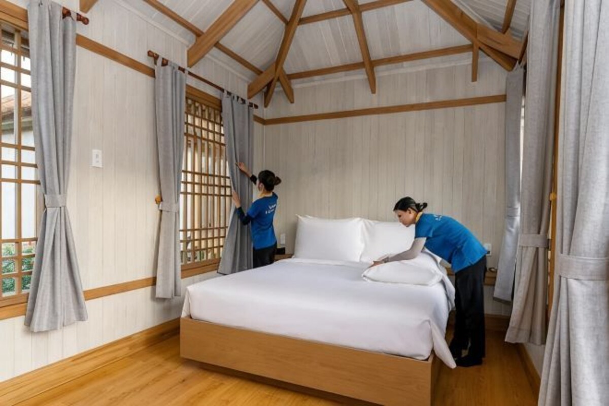 A room with a bed, wooden floor, and a window with curtains.