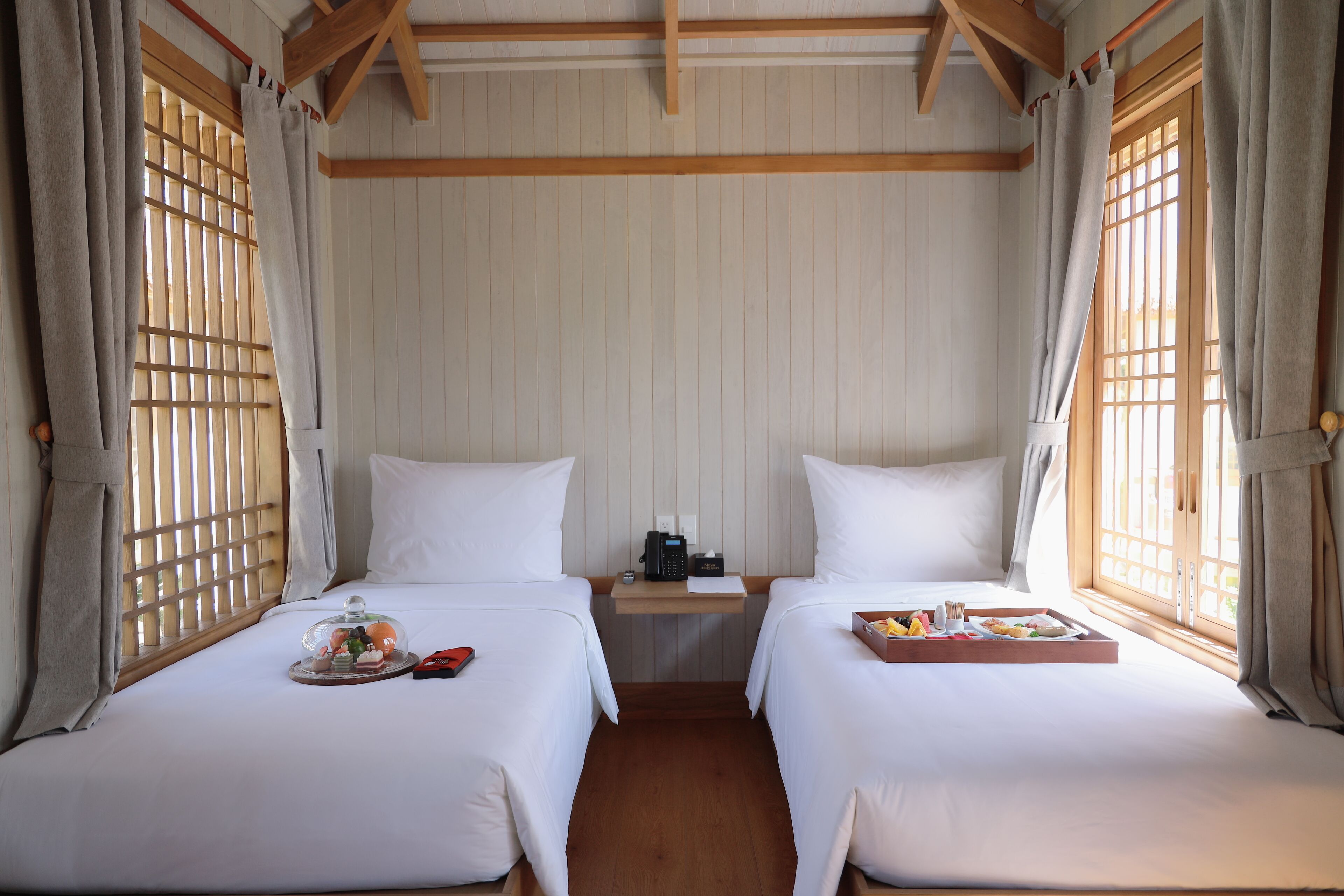 A hotel room with two beds, a wooden nightstand, and a tray with breakfast items.