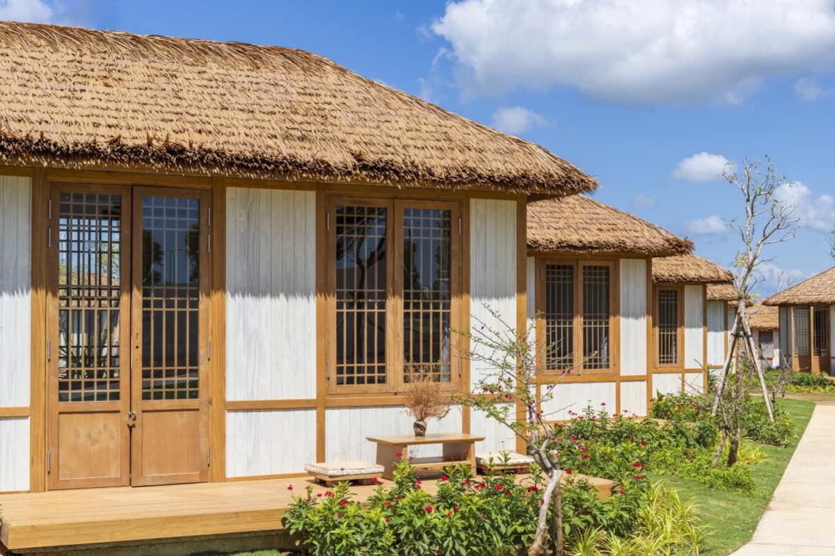A traditional-style building with a thatched roof, large windows with wooden frames, and a wooden porch.