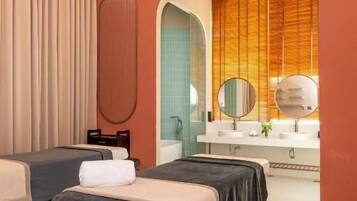 Two single beds with dark-colored bedding, a large mirror, and a vanity area with two round mirrors.