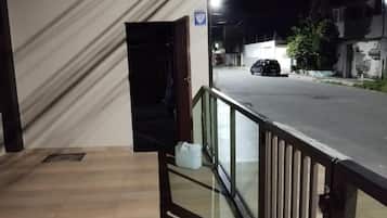 Entrada de hotel com piso de madeira, porta de vidro e vista para a rua com carros estacionados.