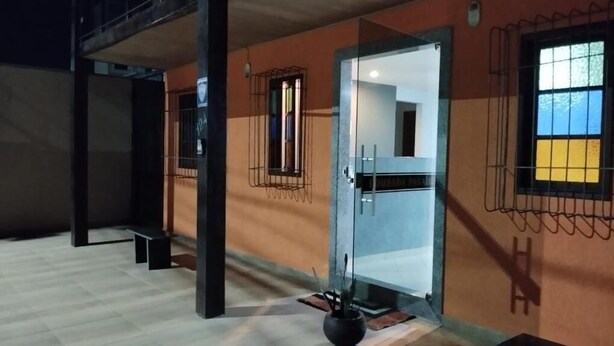 A hallway with a glass door leading to a room, a potted plant, and a bench. - Suite Pousada Paraío (Guarapari)
