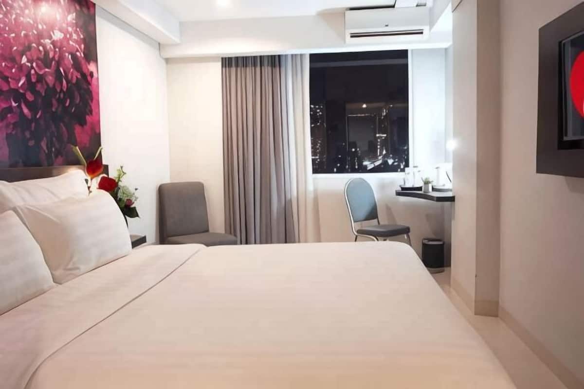 Ein Hotelzimmer mit einem großen Bett, einem Schreibtisch mit Stuhl, einem Fenster mit Blick auf die Stadt und einer Wandklimaanlage.