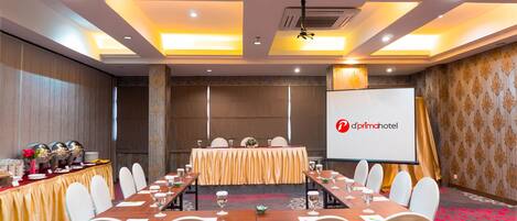 A conference room with a long table, white chairs, and a projector screen displaying the logo of 'd'primahotel'.