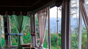 A room with large windows, a wicker chair, a small table, and a red stool.