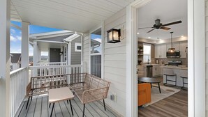 En overdækket terrasse med fletningsmøbler, et køkken med hvide skabe og moderne hårde hvidevarer, samt en loftventilator.