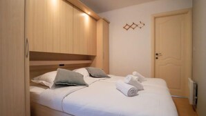 Una cama bien hecha con almohadas y toallas enrolladas, un armario de madera y una puerta con pomo.