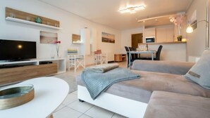 Una sala de estar moderna con una televisión de pantalla plana, un sofá, una mesa de comedor y una cocina al fondo.