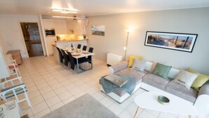 Un apartamento moderno con comedor, sala de estar con sofá y una mesa de centro, y una cocina al fondo.