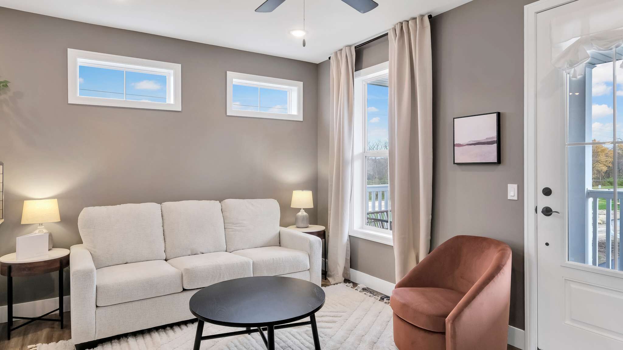 A living room with a sofa, a round table, two lamps, a chair, and a door with a view.